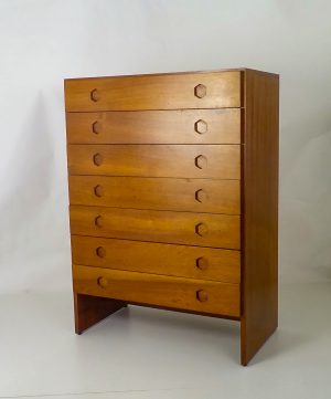 cómoda-chiffonier está hecha de madera con un tono marrón claro y acabado pulido.